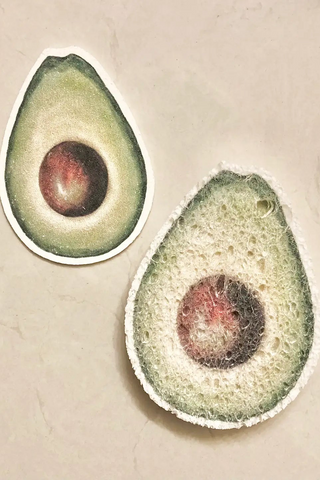 Two beige pop-up sponges with an avocado design, one whole and one cut in half, on a sustainable background.