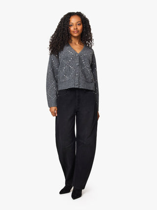 A model stands against a light gray studio background wearing a gray knit cardigan with small white speckled details, black wide-leg pants, and black pointed shoes.