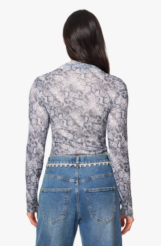 A woman shown from the back wearing a fitted long-sleeve top with a gray and white snakeskin pattern, paired with blue jeans featuring a decorative silver chain detail at the waistband, against a plain white background.
