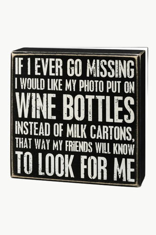 Black box sign with white text humorously suggesting to put a photo on wine bottles for missing friends.