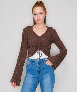 A woman modeling a brown long-sleeve knit cropped top with a V-neck, front ruching, and drawstring tie, paired with blue jeans.