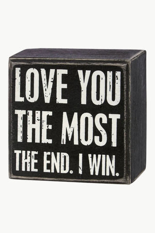 Black wooden block with white text 'LOVE YOU THE MOST THE END. I WIN.'
