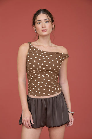 Woman wearing a brown one-shoulder top with cream white polka dots.