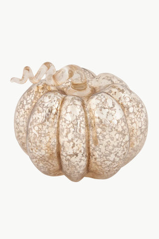 A decorative glass pumpkin with a ribbed design, featuring a mottled, metallic gold and champagne finish with a matching wavy stem, set against a plain white background.