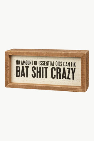 Wooden box sign with text 'No amount of essential oils can fix bat shit crazy' on a white background